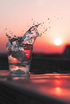 Cup of filtered water splashing in front of a sunset.